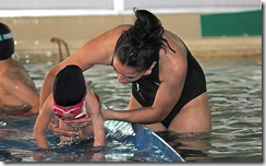 Una monitora sujeta a un niño que practica ejecricios en el agua